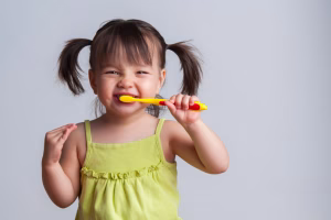 A girl with pig tails holding a toothbrush in her mouth.